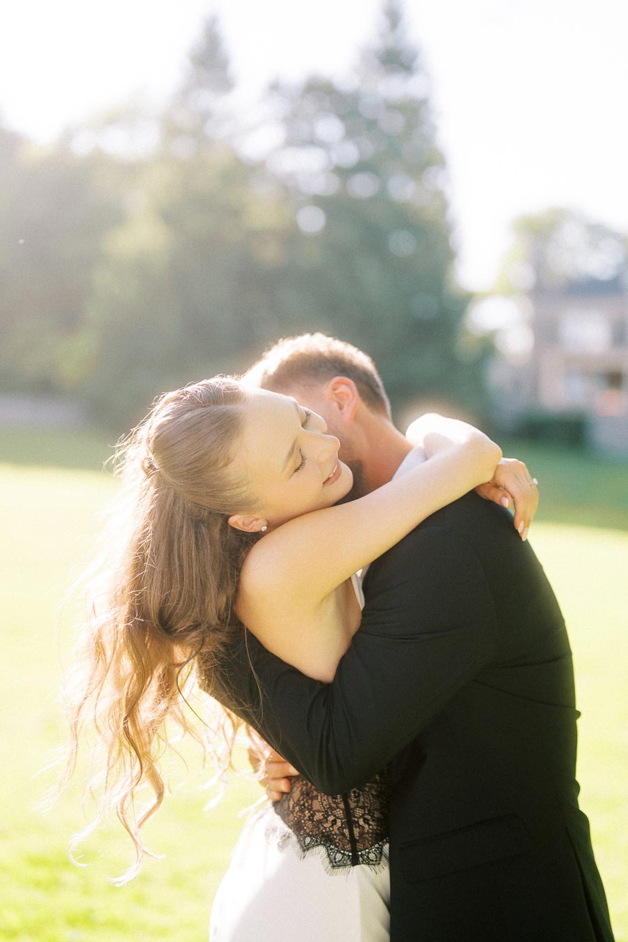 Engaged couple hugging closely in bright outdoor garden with sunlight and blurred trees.
