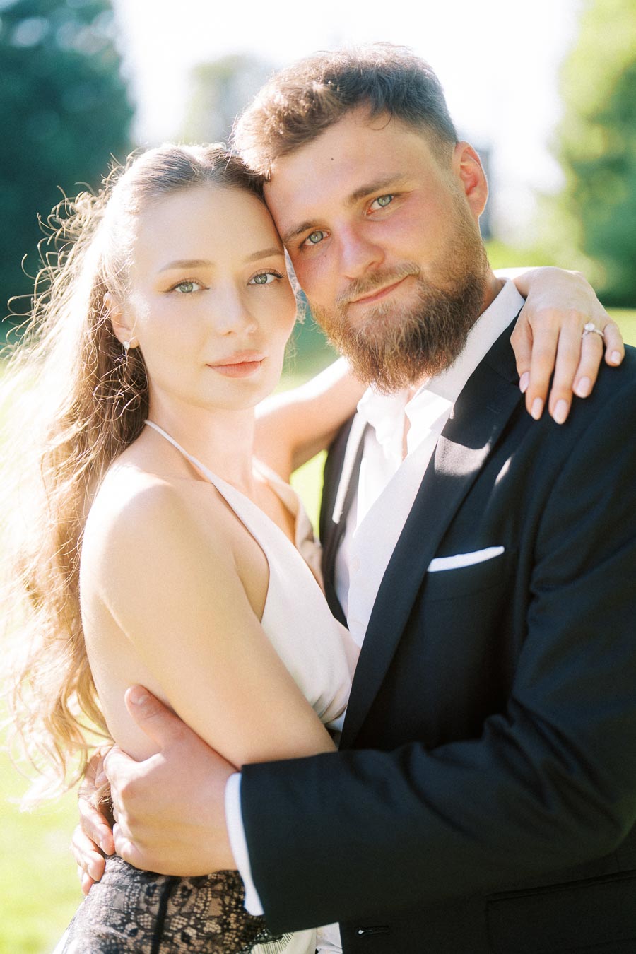Anastasiia and Petr embracing closely, both looking at the camera, with sunlight highlighting their faces and Anastasiia's ring visible.