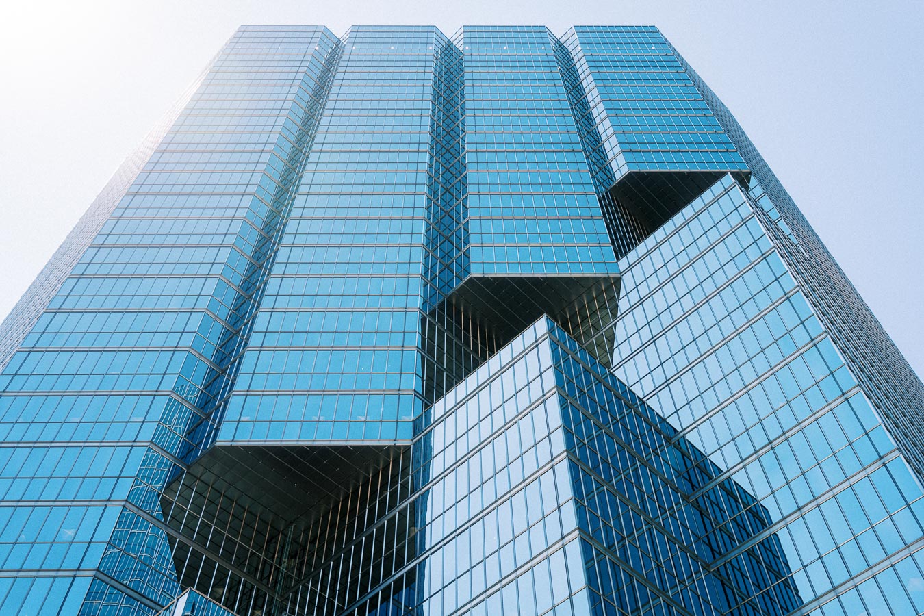 Looking up at a modern glass office tower in downtown Toronto with geometric architecture and reflective blue windows.