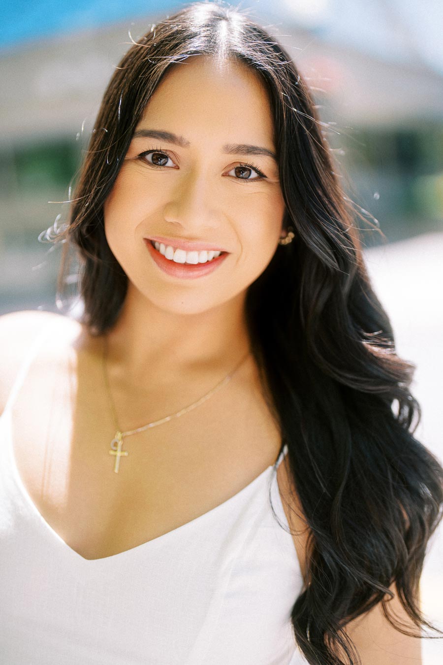 Cassie smiling at the camera during her engagement session in downtown Toronto, wearing a white dress and gold necklace.