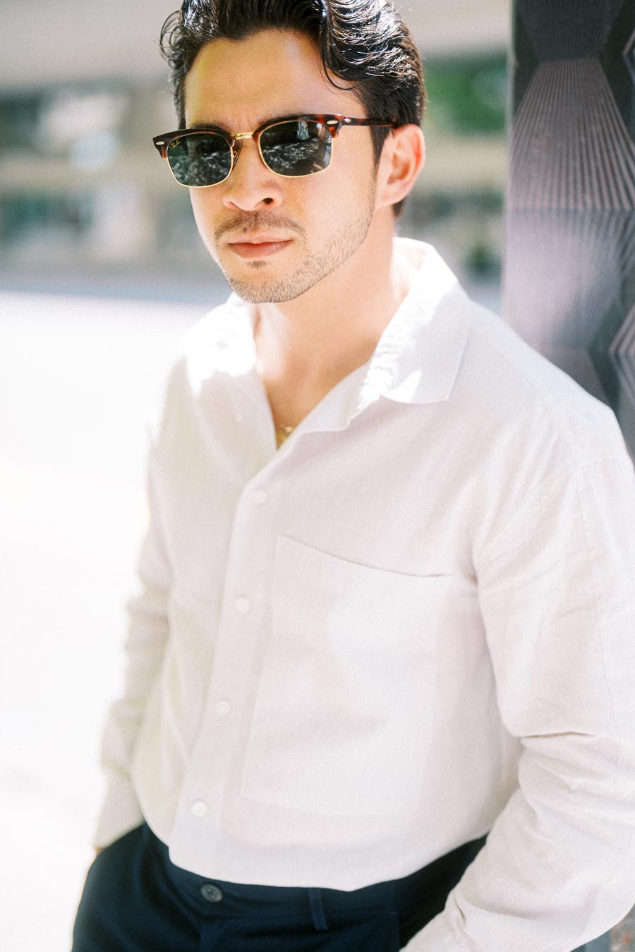 Gabriel wearing sunglasses and a white shirt, leaning against a textured wall in downtown Toronto.