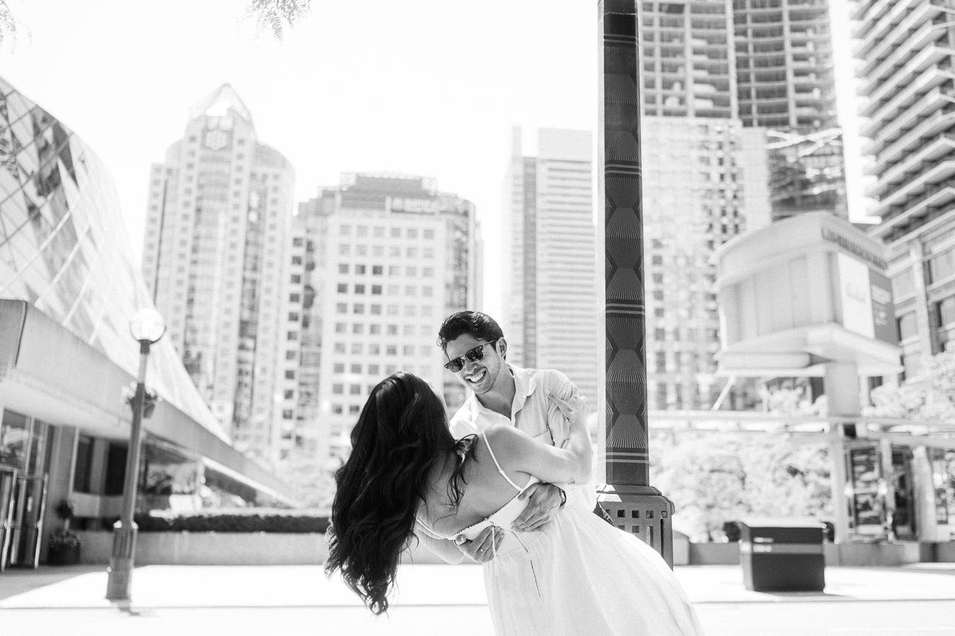 Cassie and Gabriel dancing together in an outdoor urban setting with tall buildings in downtown Toronto.