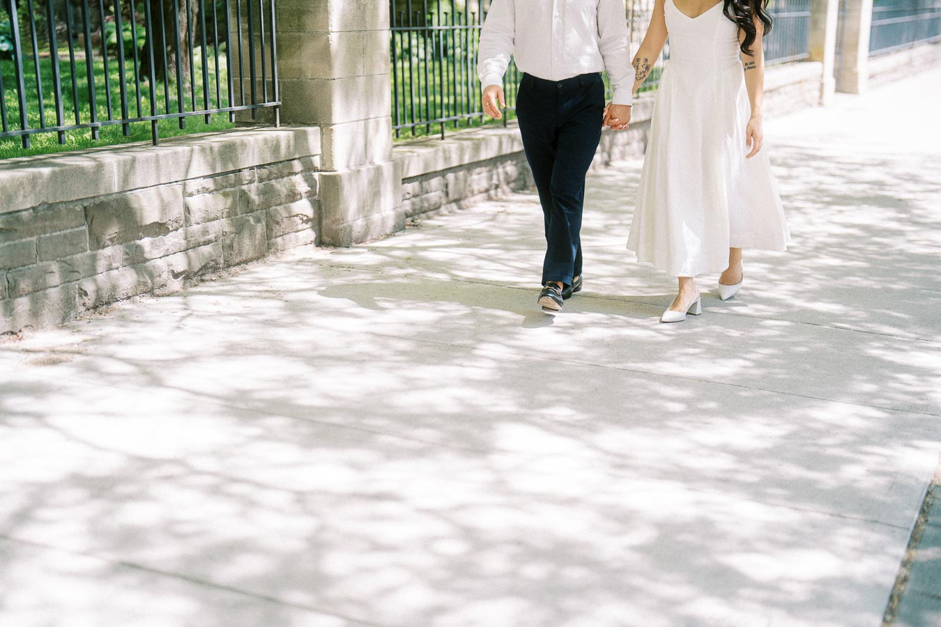 A couple holding hands and walking together on a shaded downtown Toronto sidewalk, with only their lower bodies visible.