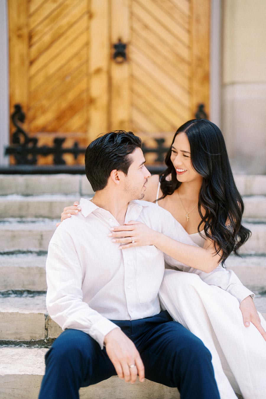 Cassie and Gabriel sitting closely together on stone steps in downtown Toronto, smiling at each other in front of a wooden door.