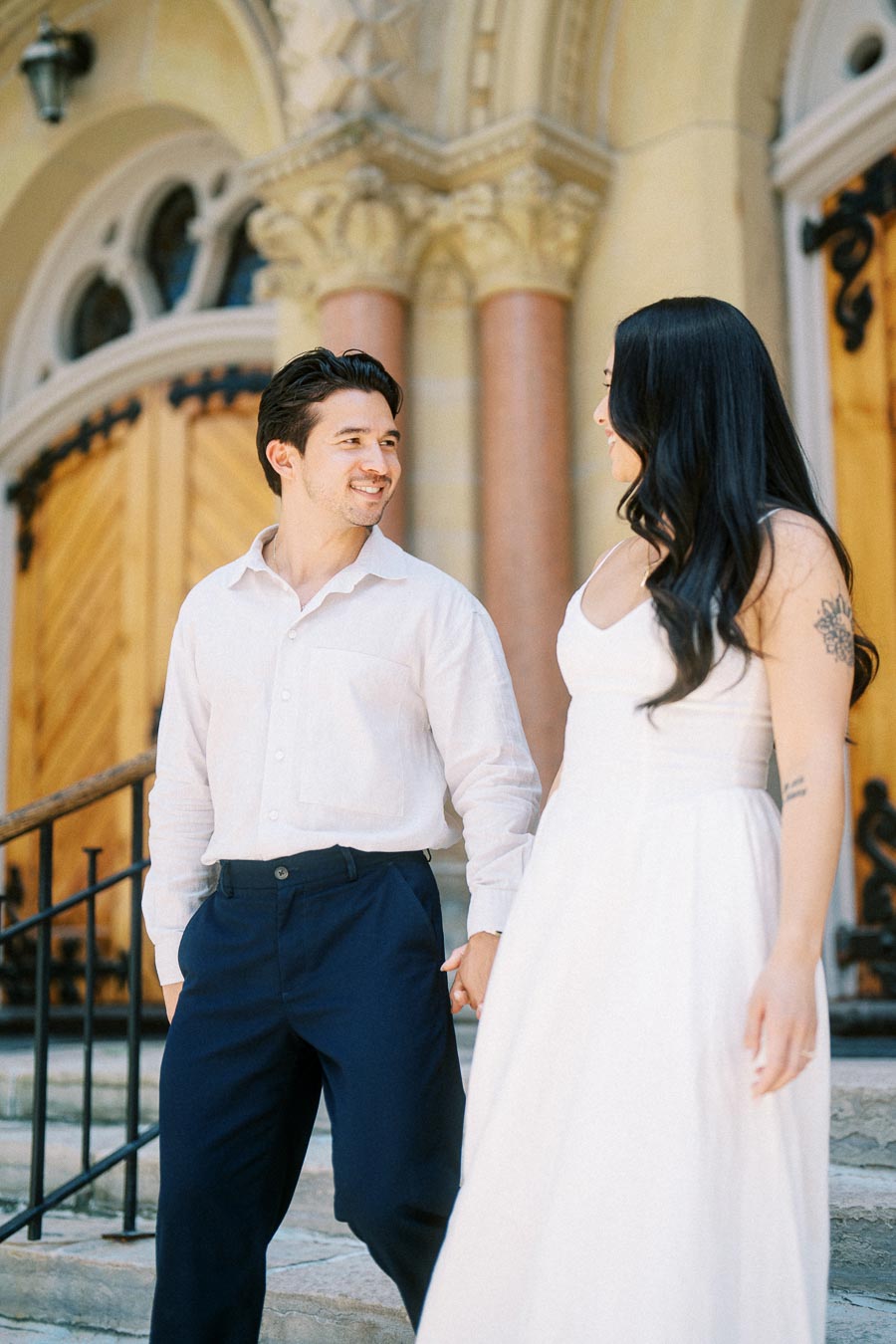 Cassie and Gabriel holding hands and smiling at each other on the stone steps of a historic building in downtown Toronto.