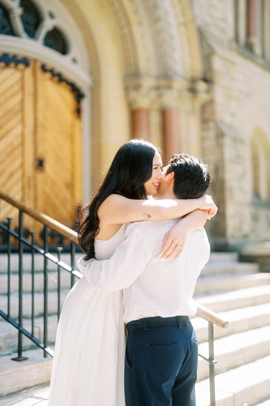 Cassie and Gabriel hugging on stone steps outside a historic church in downtown Toronto during their engagement session.