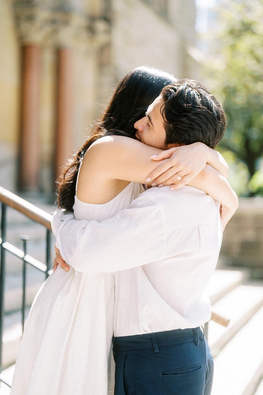 Cassie and Gabriel hugging closely on sunlit stone steps during their engagement photoshoot in downtown Toronto.