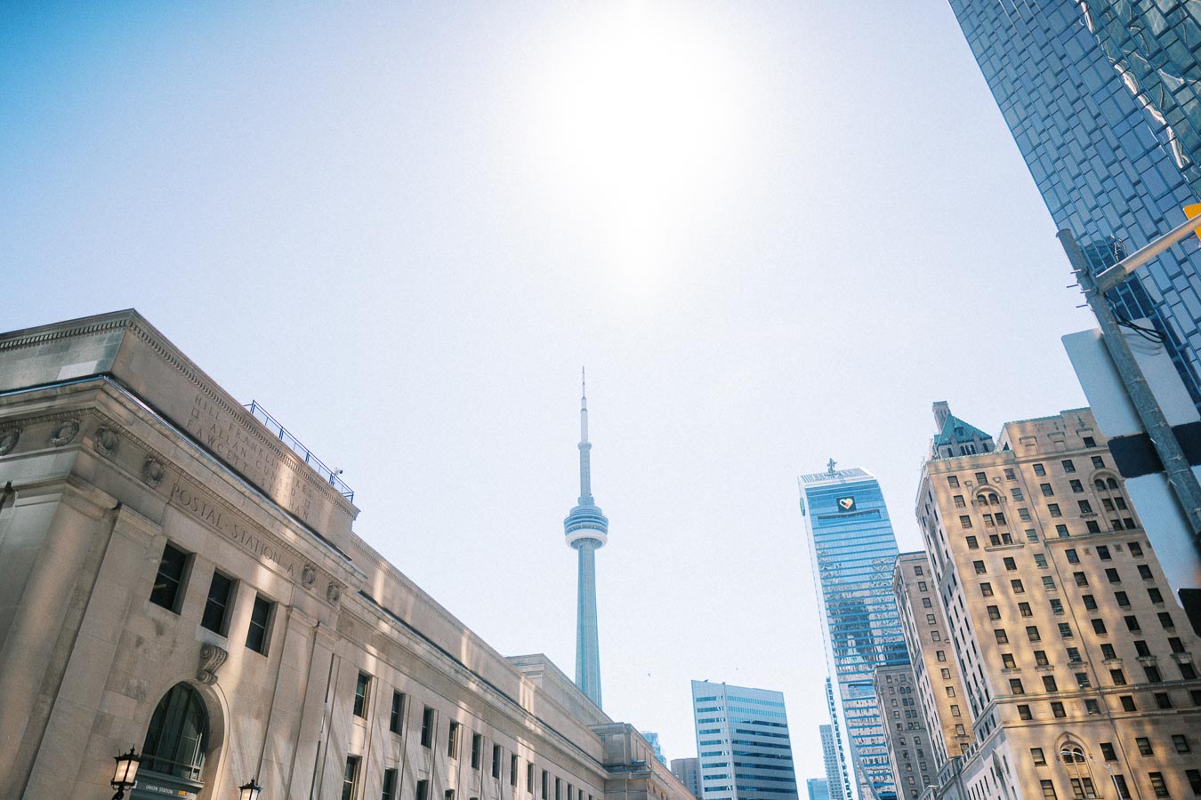 Downtown Toronto cityscape with the CN Tower in the center, Union Station on the left, and surrounding skyscrapers under a clear sky.