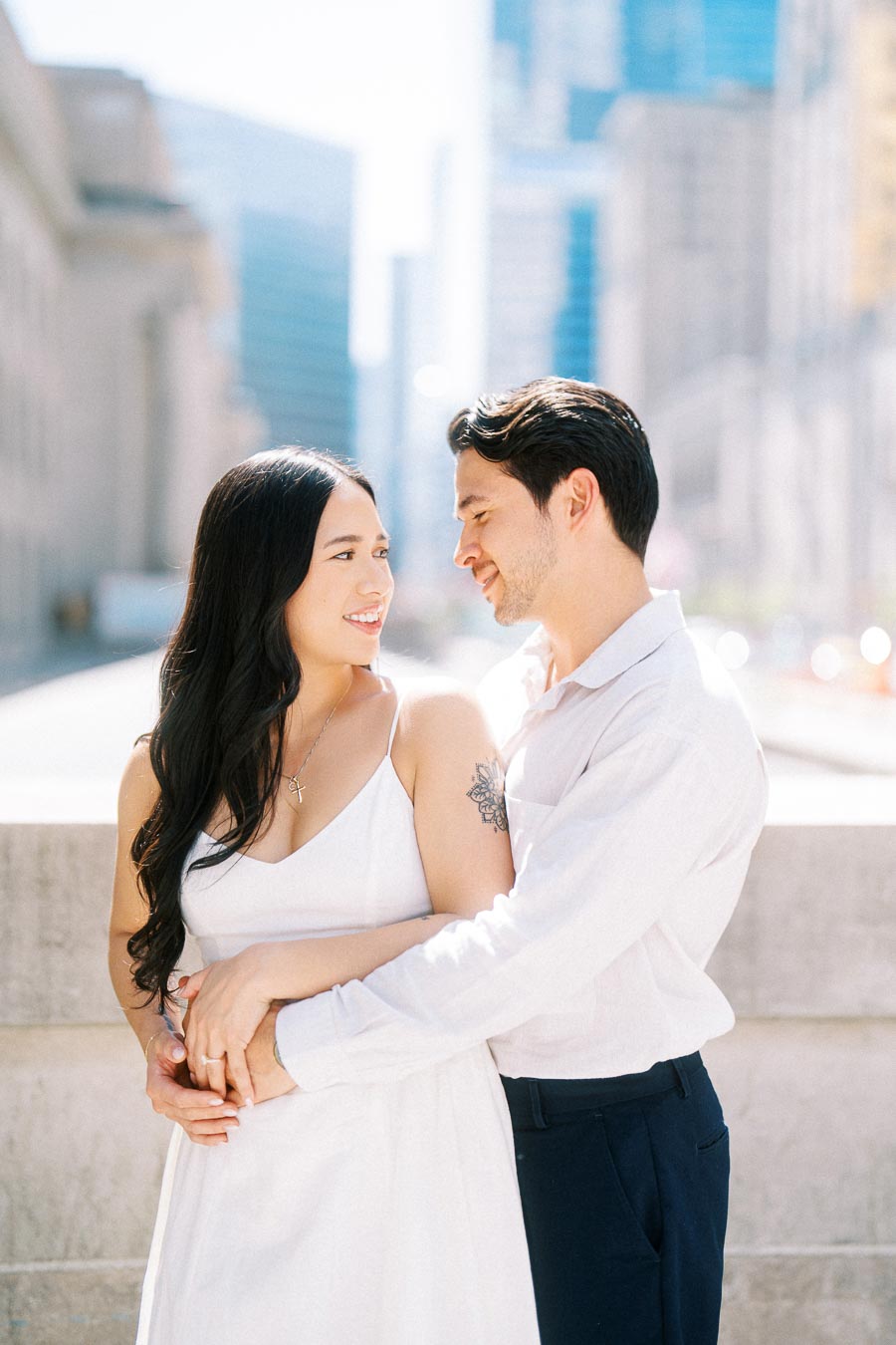 Cassie and Gabriel smiling and embracing each other during their engagement photoshoot on a bright downtown Toronto street.