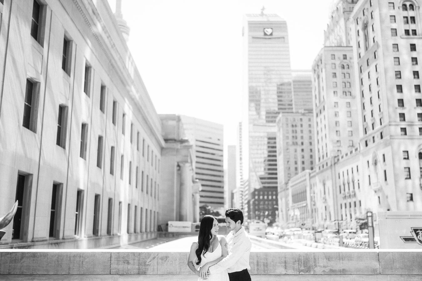 Cassie and Gabriel stand close together on a city street in downtown Toronto, framed by historic and modern buildings.