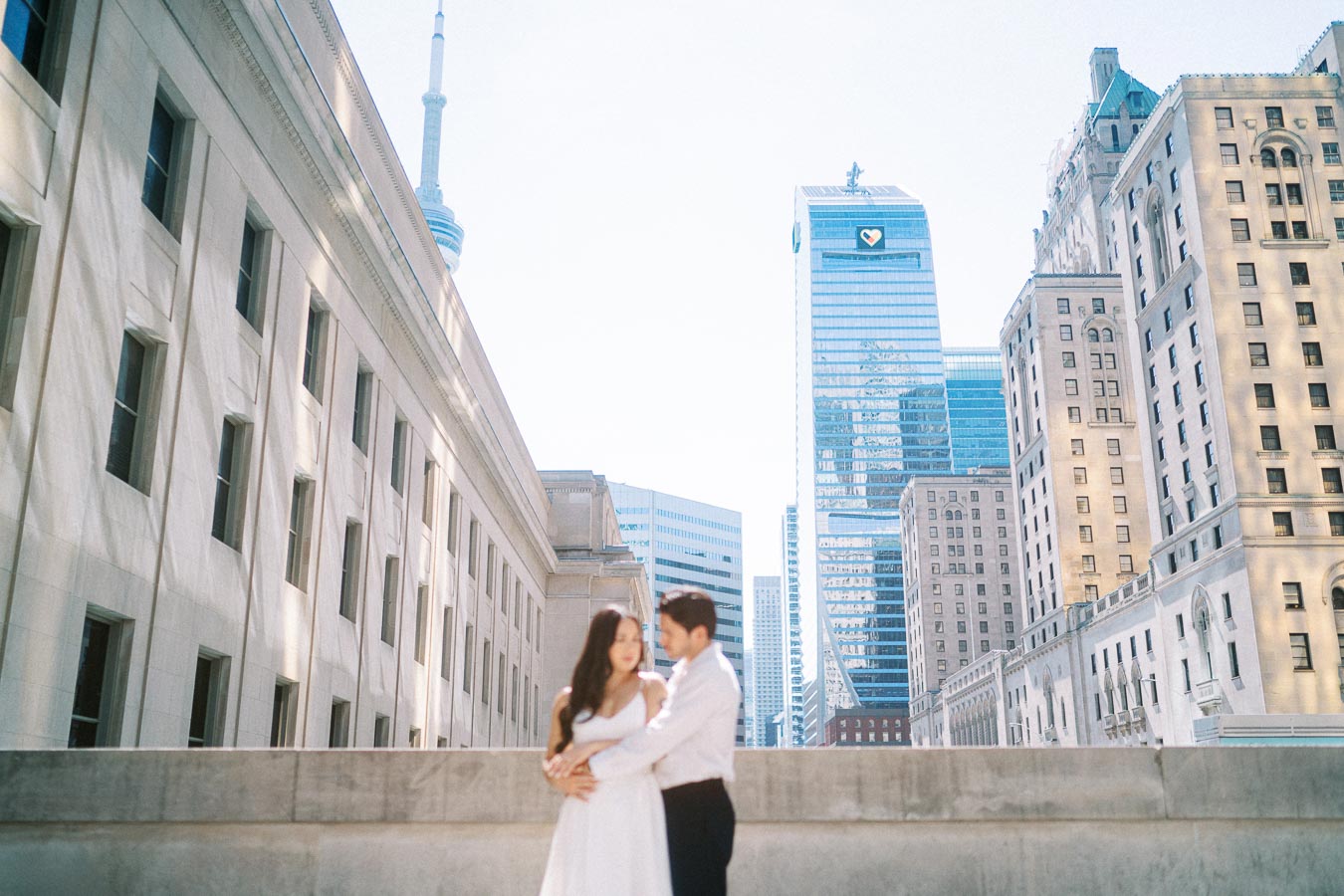Cassie and Gabriel standing close together during their engagement session, with the CN Tower and Toronto city skyline visible behind them.
