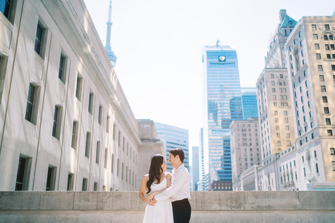 Cassie and Gabriel stand together on a downtown Toronto street, holding each other with the CN Tower and city buildings behind them.