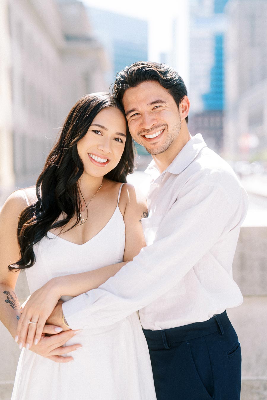 Cassie and Gabriel smiling and embracing each other during their engagement photoshoot in downtown Toronto, with city buildings in the background.
