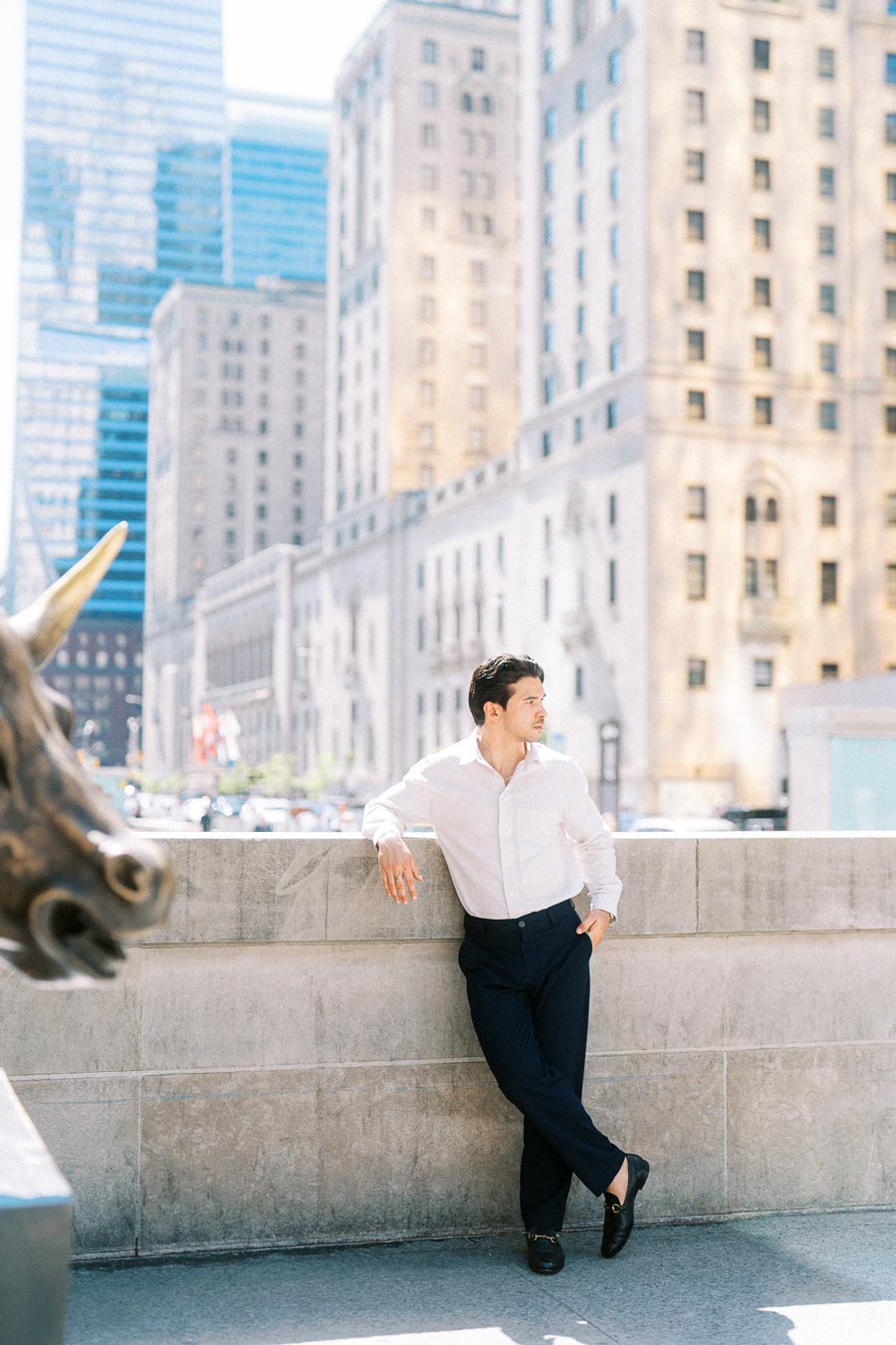 Gabriel leans against a stone wall in downtown Toronto, with tall historic buildings and a bull statue visible nearby.