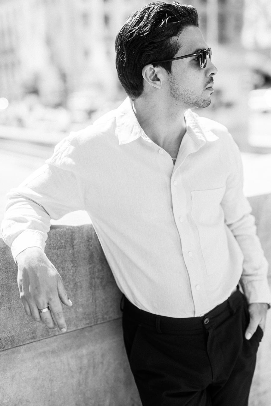 A man in a light shirt and sunglasses leans against a stone railing in downtown Toronto, photographed in black and white.