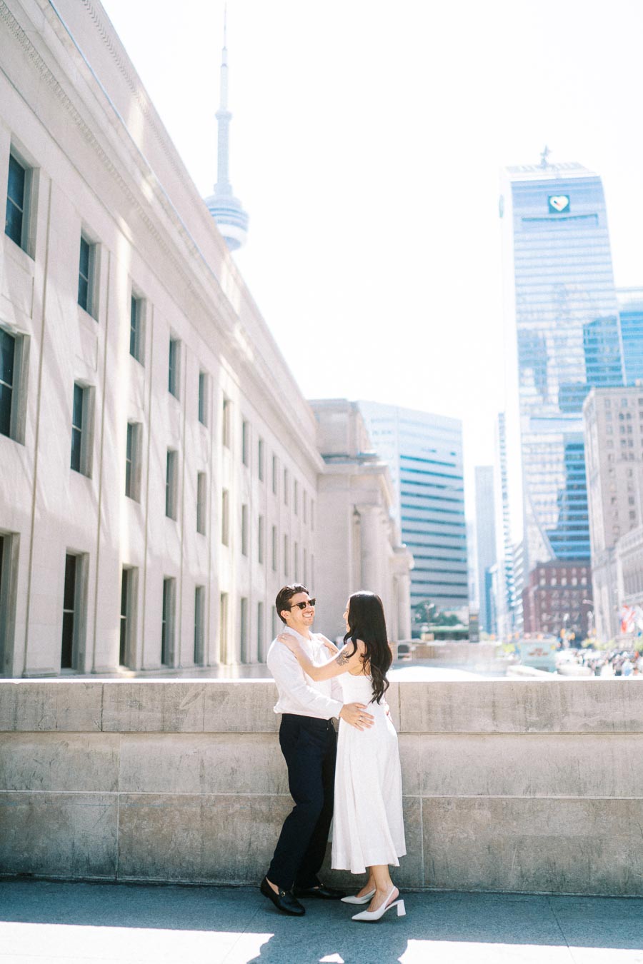 Cassie and Gabriel smiling and embracing outside Union Station in downtown Toronto, with the CN Tower and city buildings visible behind them.