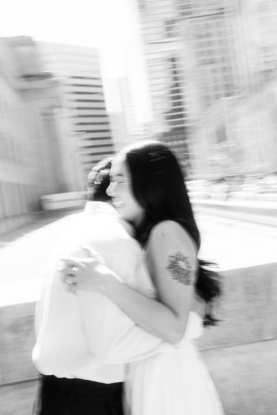 Cassie and Gabriel embracing and smiling during their engagement session with blurred downtown Toronto buildings in the background.