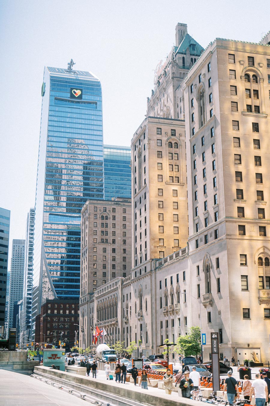 Street view in downtown Toronto showing historic stone buildings alongside modern glass skyscrapers with people and traffic below.