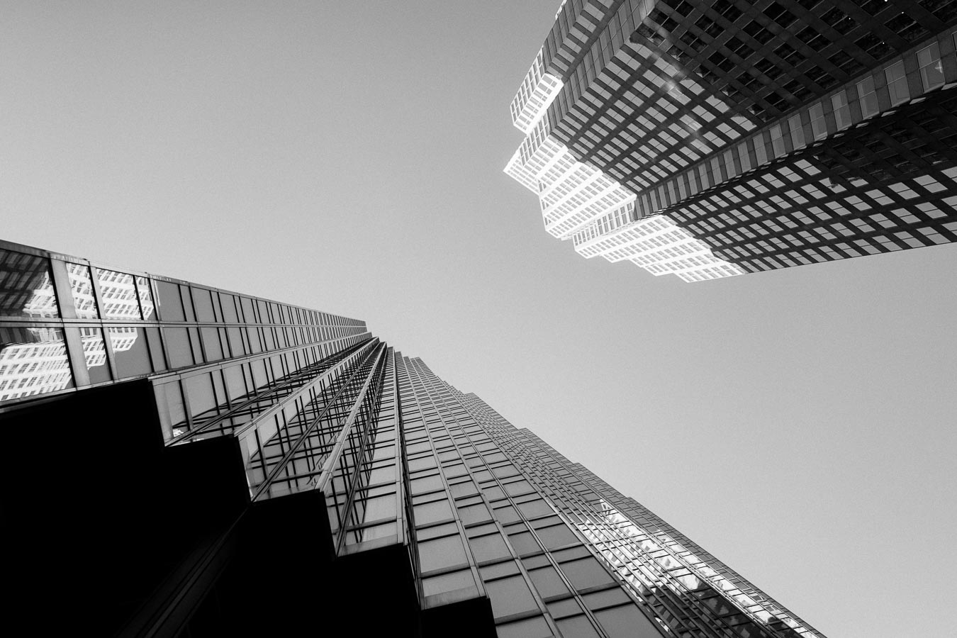 Black and white photo looking up at two tall glass office towers in downtown Toronto against a clear sky.
