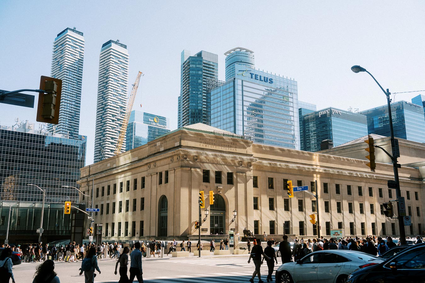 A busy city street scene in downtown Toronto with crowds crossing in front of Union Station and glass skyscrapers in the background.