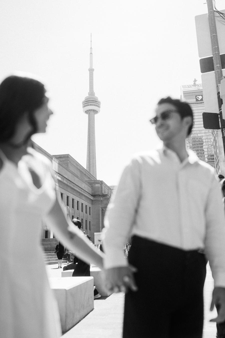 Cassie and Gabriel holding hands in the foreground with the CN Tower visible in the background during their engagement session in downtown Toronto.