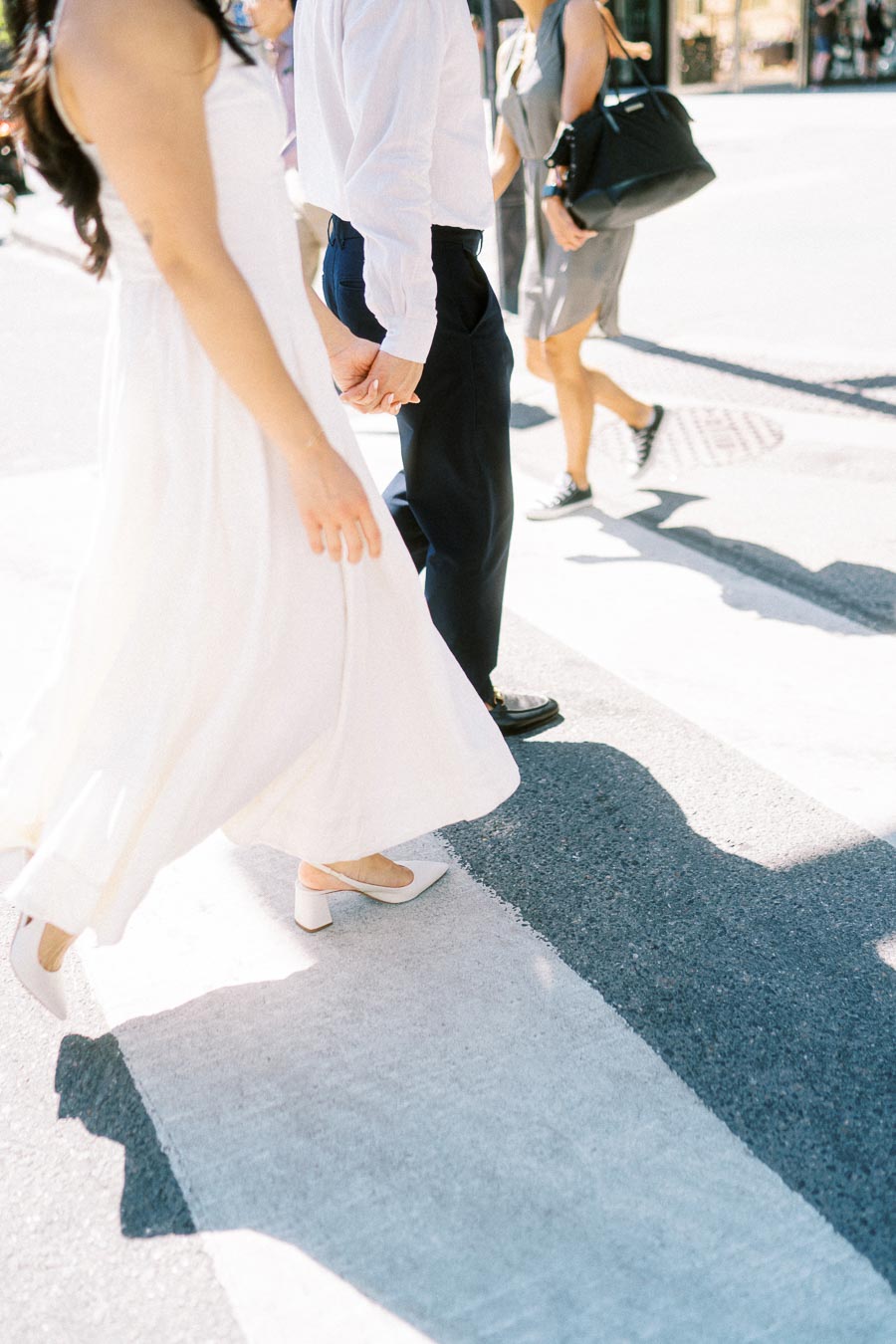 Cassie and Gabriel holding hands while walking across a crosswalk in downtown Toronto during their engagement session.