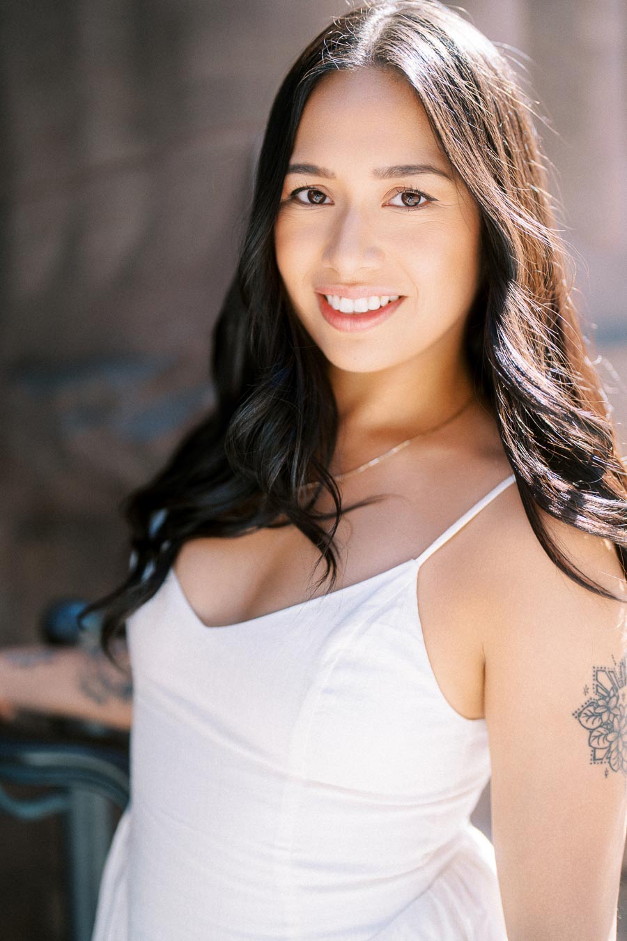 Cassie smiling in a close-up engagement portrait outdoors in downtown Toronto, wearing a white dress with sunlight on her hair.