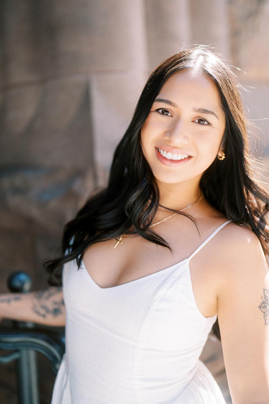 Cassie smiling in a white dress during her engagement session, standing in front of historic stone architecture in downtown Toronto.