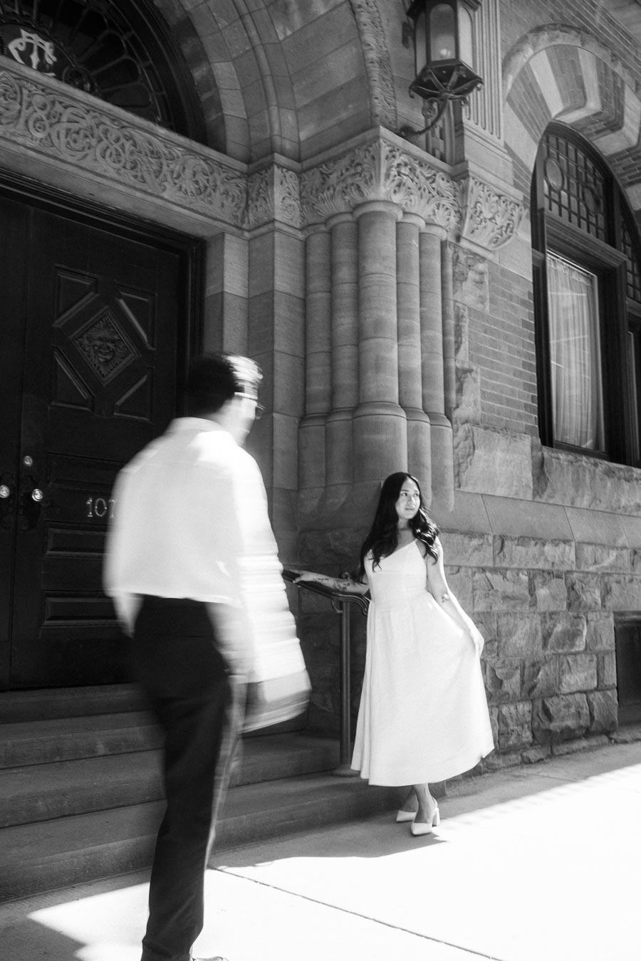Cassie and Gabriel stand on the stone steps of a historic building in downtown Toronto during their engagement photoshoot.