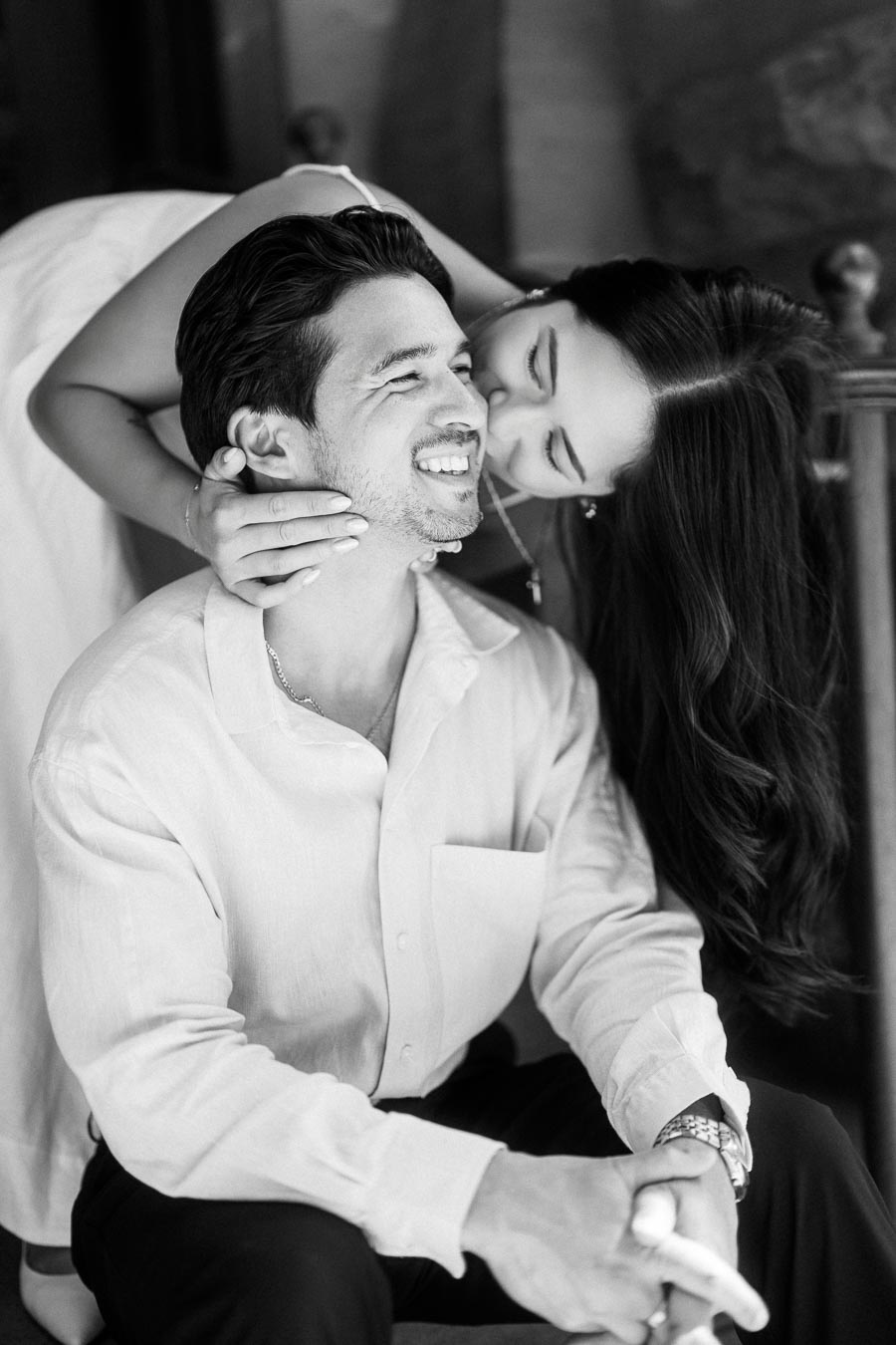 Cassie embraces Gabriel from behind and kisses his cheek while he smiles, photographed during their engagement session in downtown Toronto.