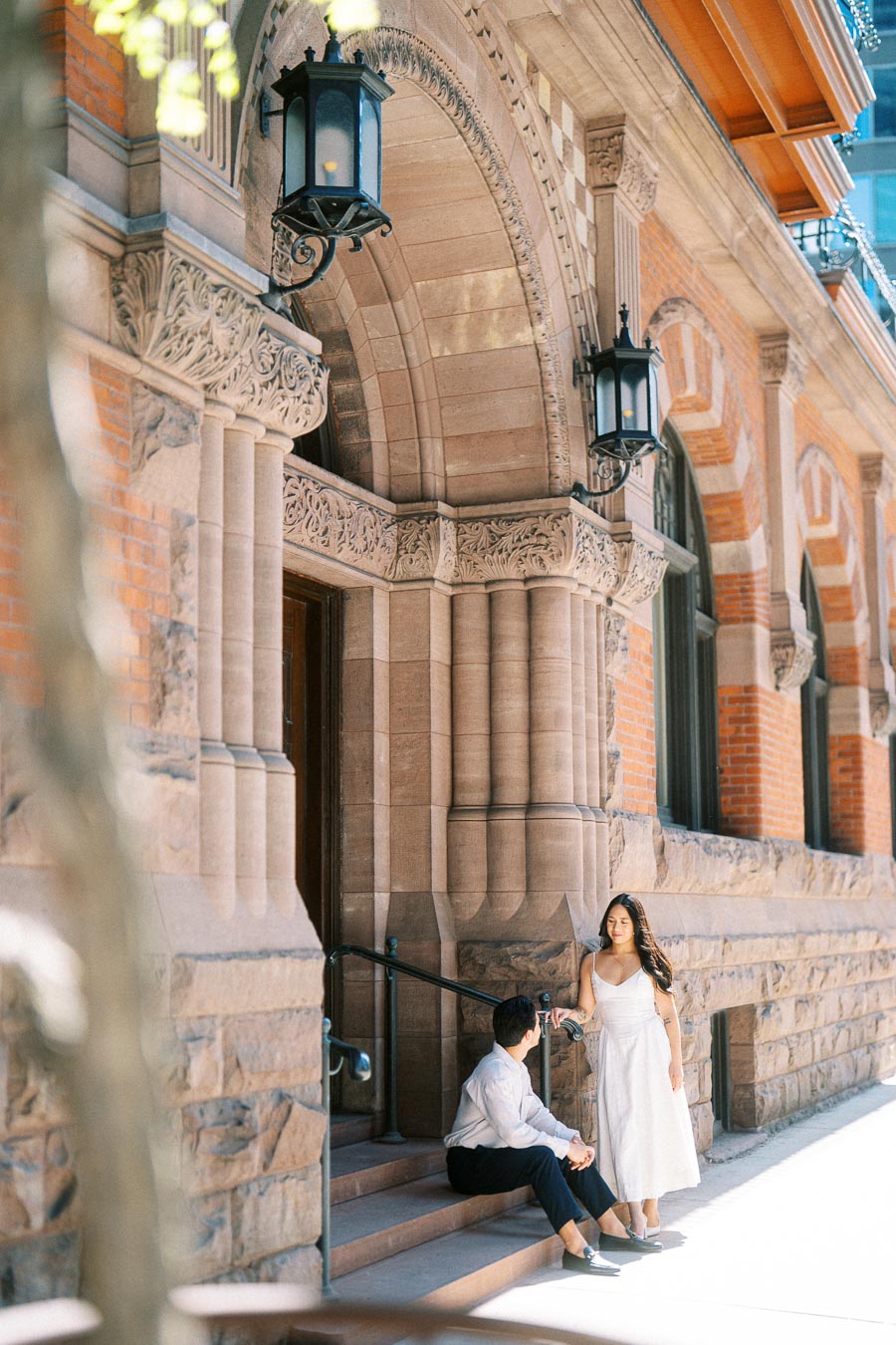 Cassie and Gabriel pose together on the stone steps of a historic building in downtown Toronto during their engagement session.
