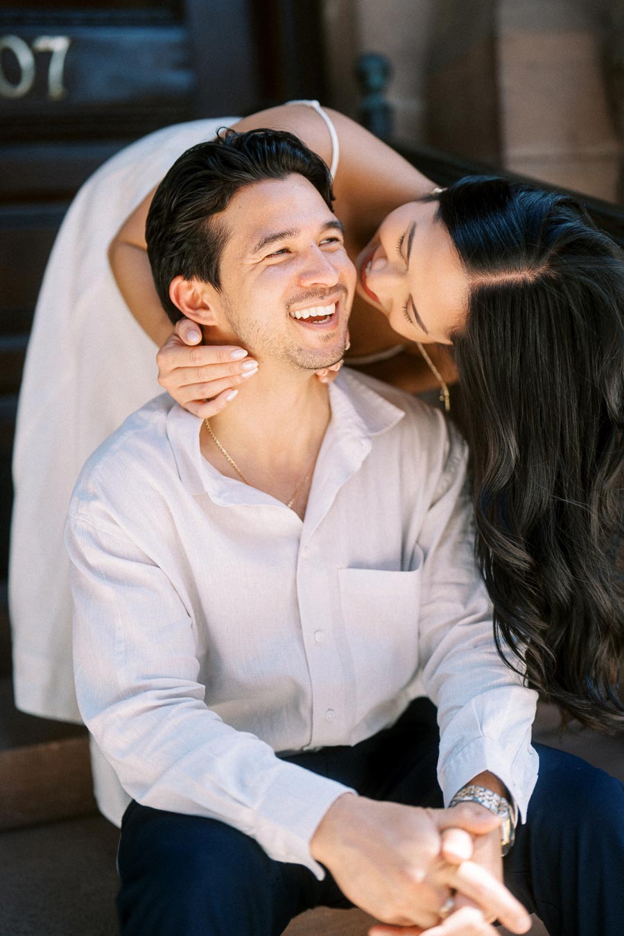 Cassie leans over Gabriel from behind, embracing him and smiling together on stone steps in downtown Toronto.