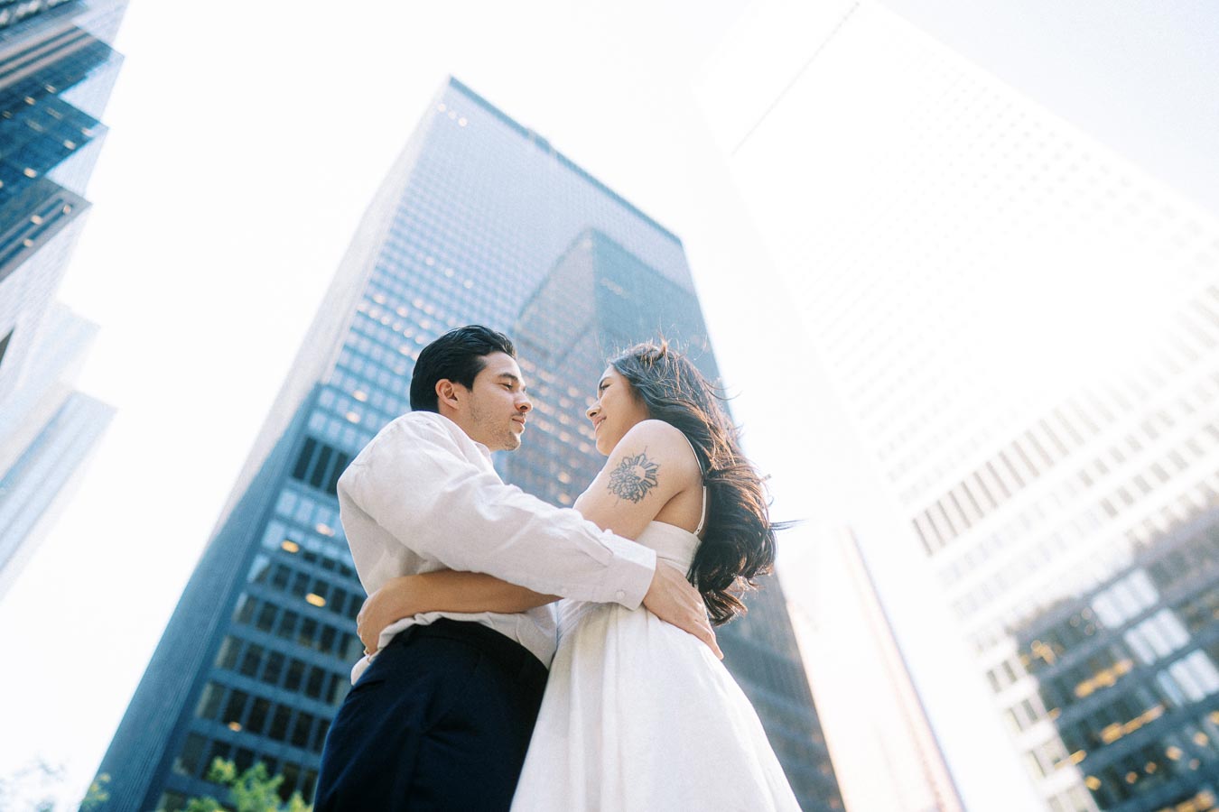 Cassie and Gabriel embracing and looking at each other, standing among tall glass and steel buildings in downtown Toronto.