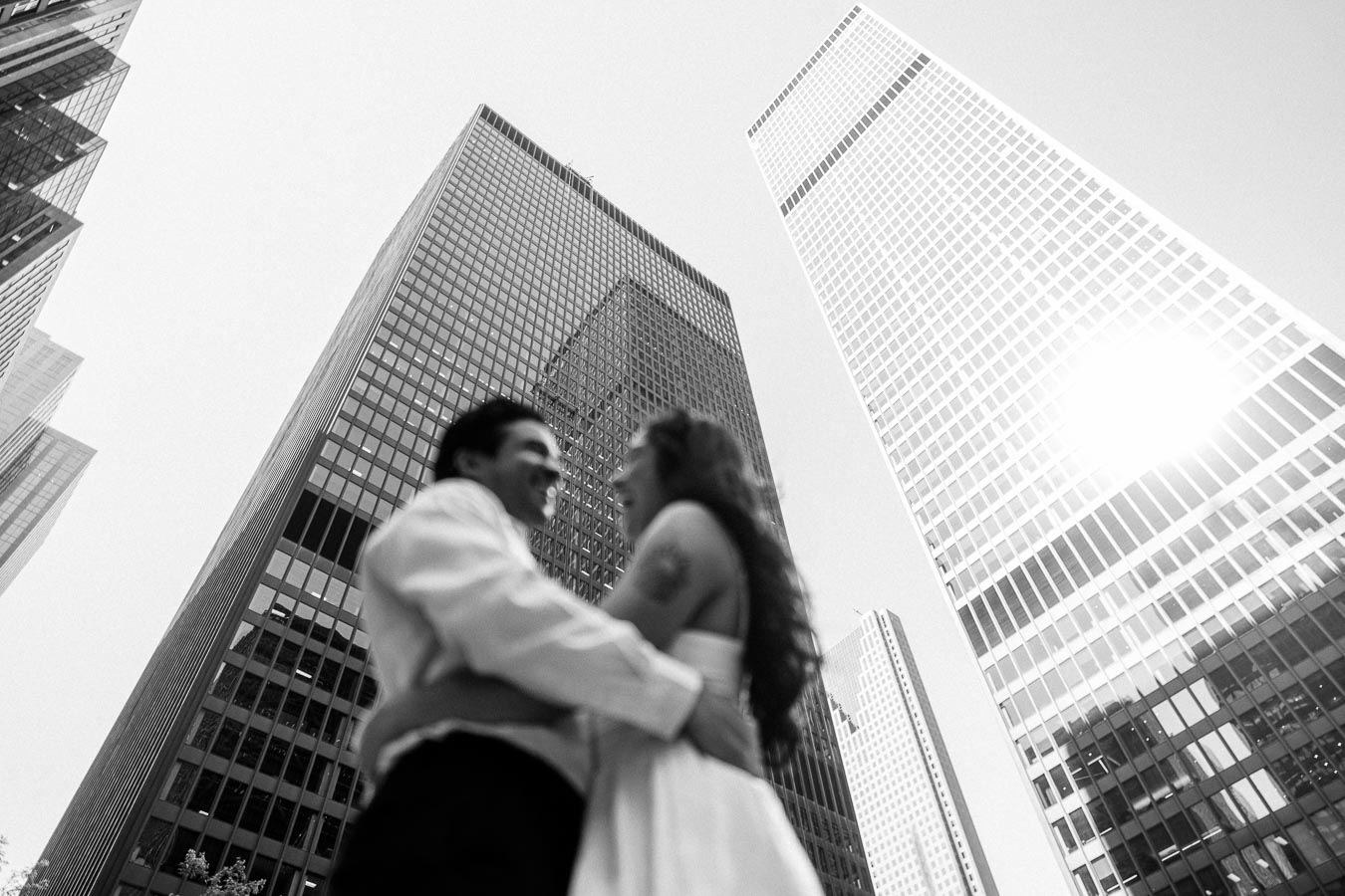 Cassie and Gabriel embracing and smiling with tall glass office towers in downtown Toronto in the background.