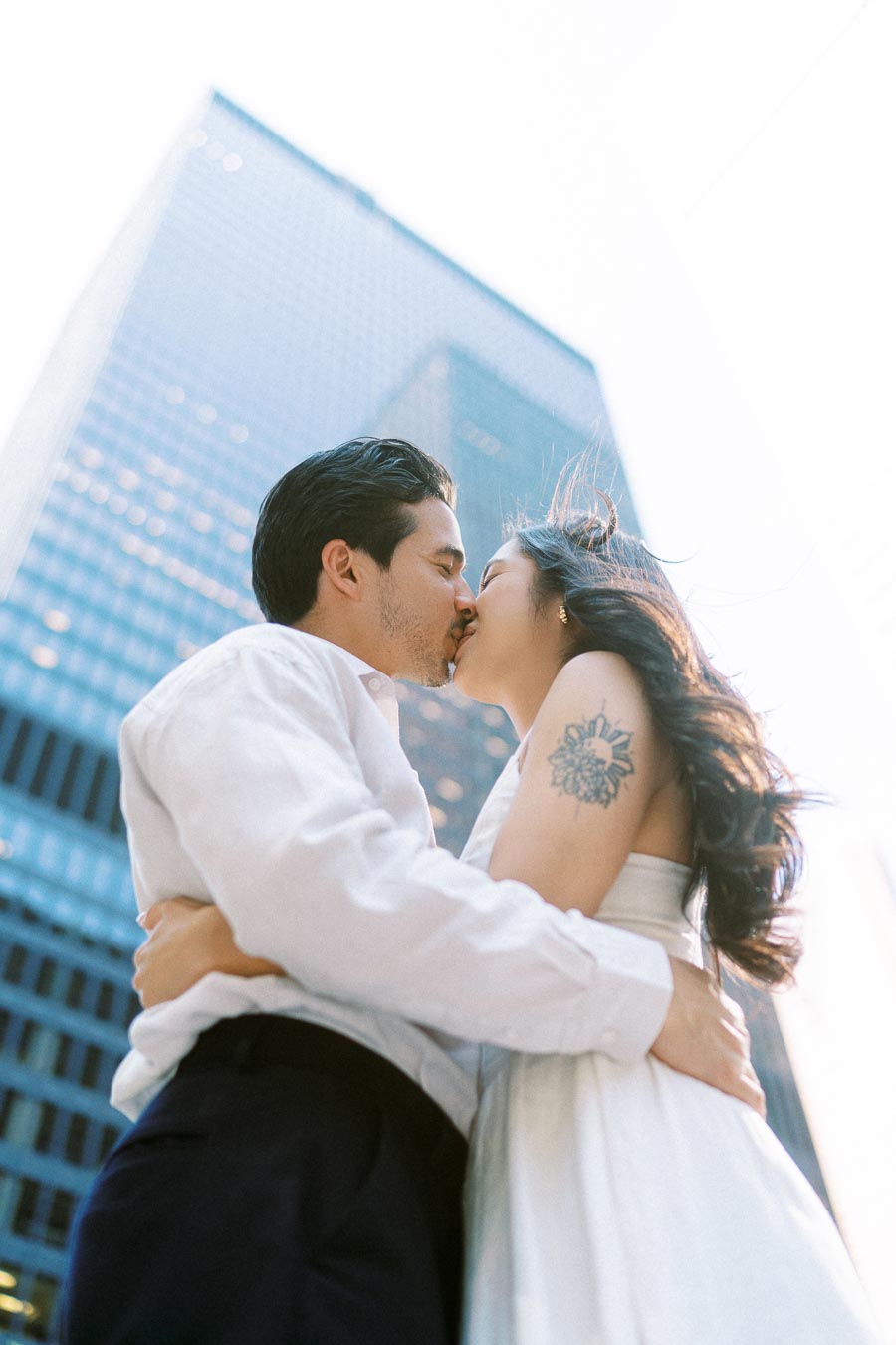 Cassie and Gabriel kissing during their engagement photoshoot, with modern glass skyscrapers in downtown Toronto in the background.