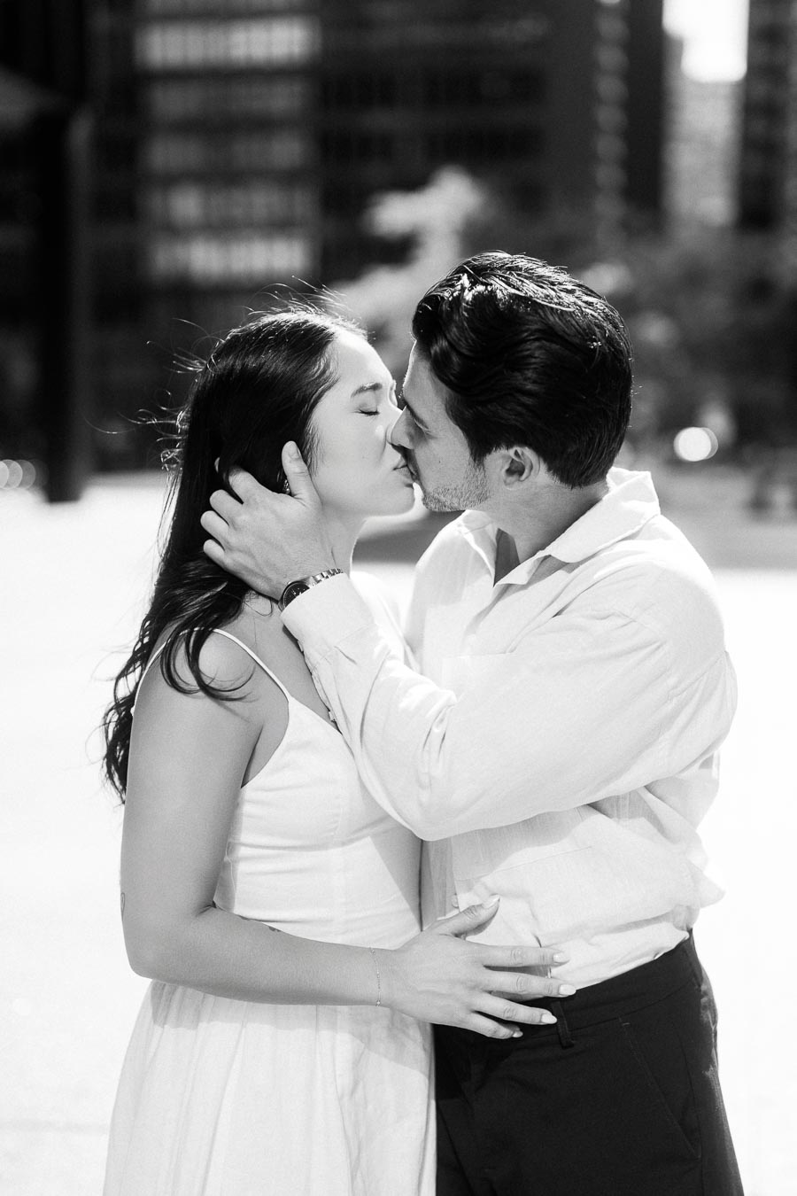 Cassie and Gabriel kissing during their engagement session in downtown Toronto, with blurred city buildings in the background.