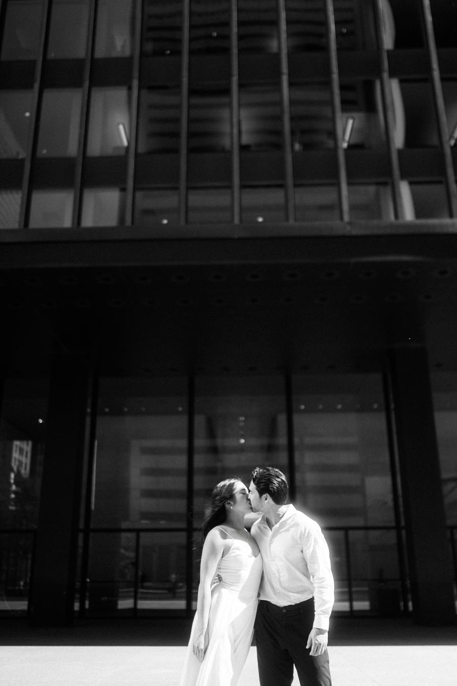Cassie and Gabriel kissing in front of a modern glass office building during their engagement session in downtown Toronto.