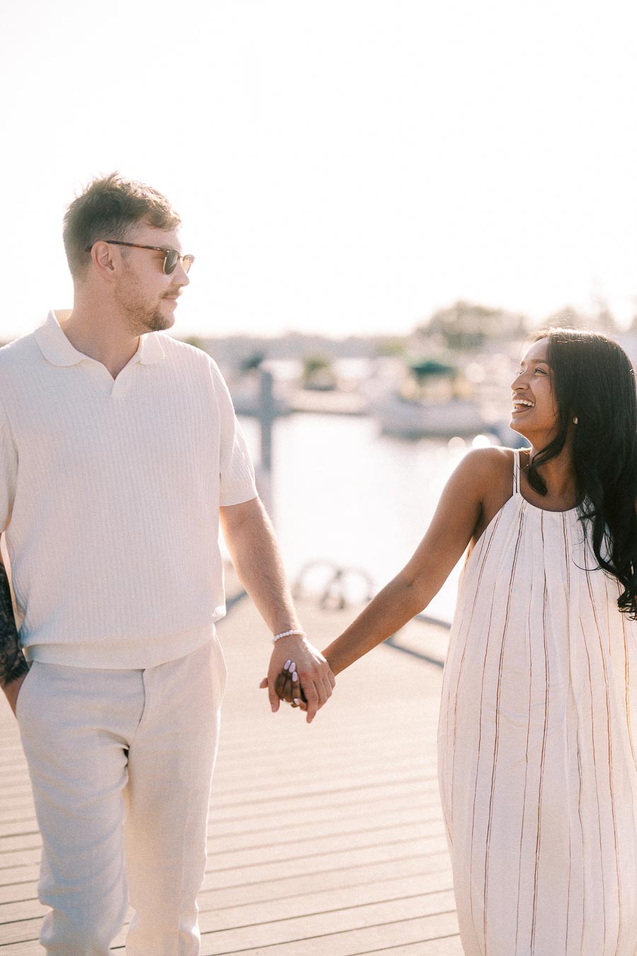 Amber and Devin holding hands on a marina dock during a warm engagement session in Hamilton.