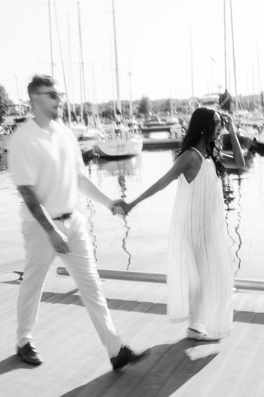 Amber and Devin walking hand in hand on a marina dock with sailboats behind them.