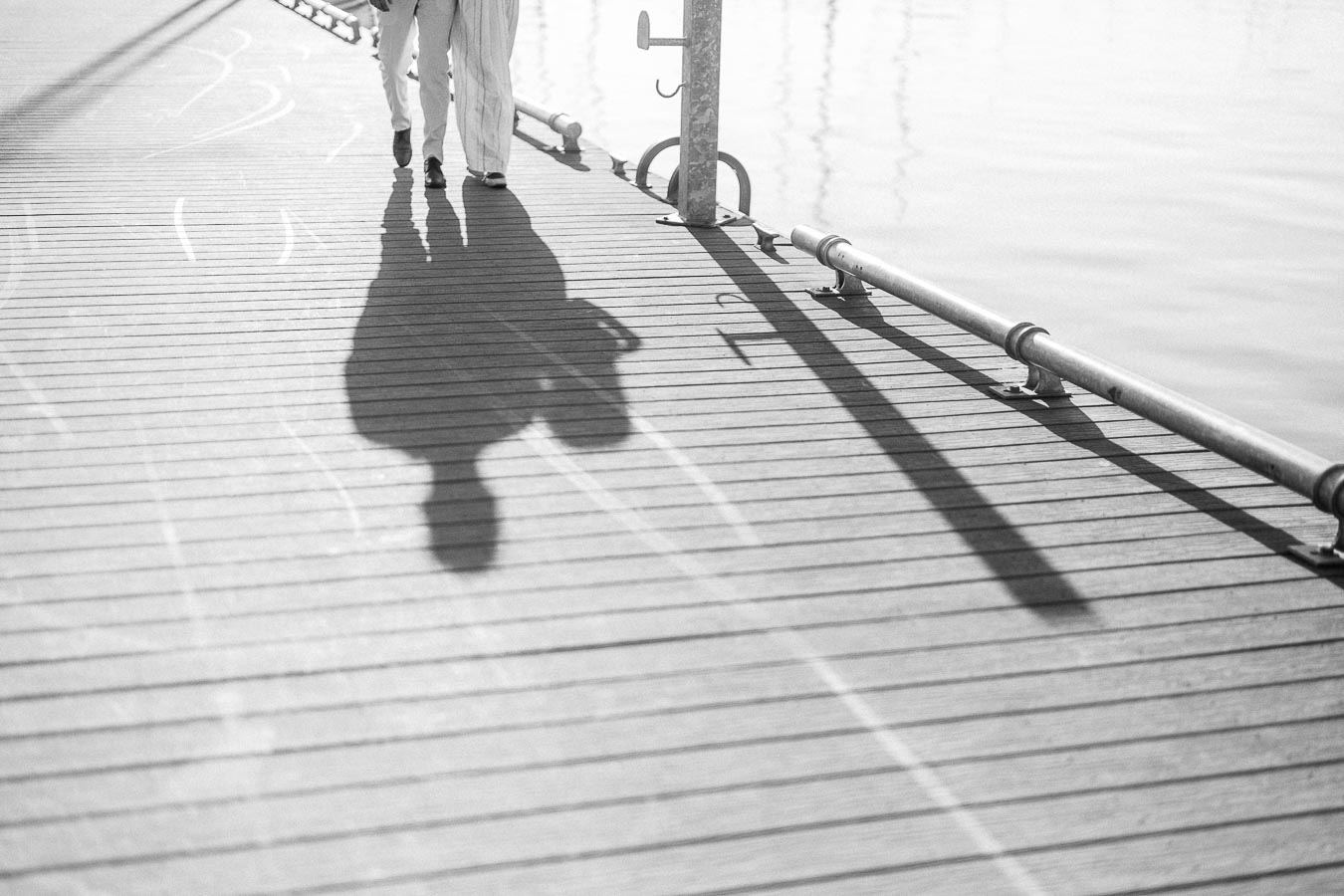 Couple’s shadows stretch across a marina dock during a waterfront engagement session in Hamilton.