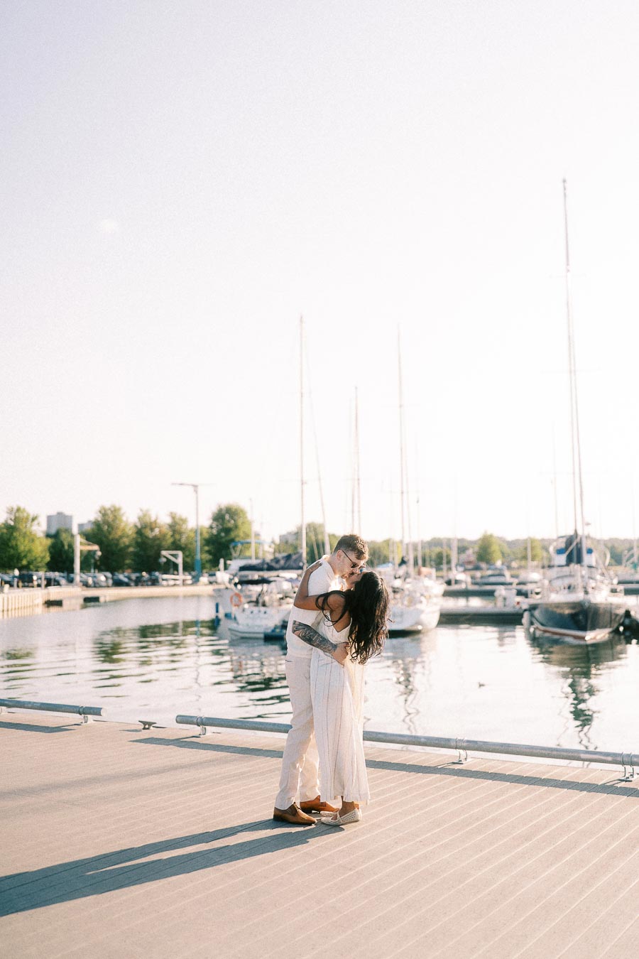 Amber and Devin kissing on a marina dock with sailboats in Hamilton, Ontario.