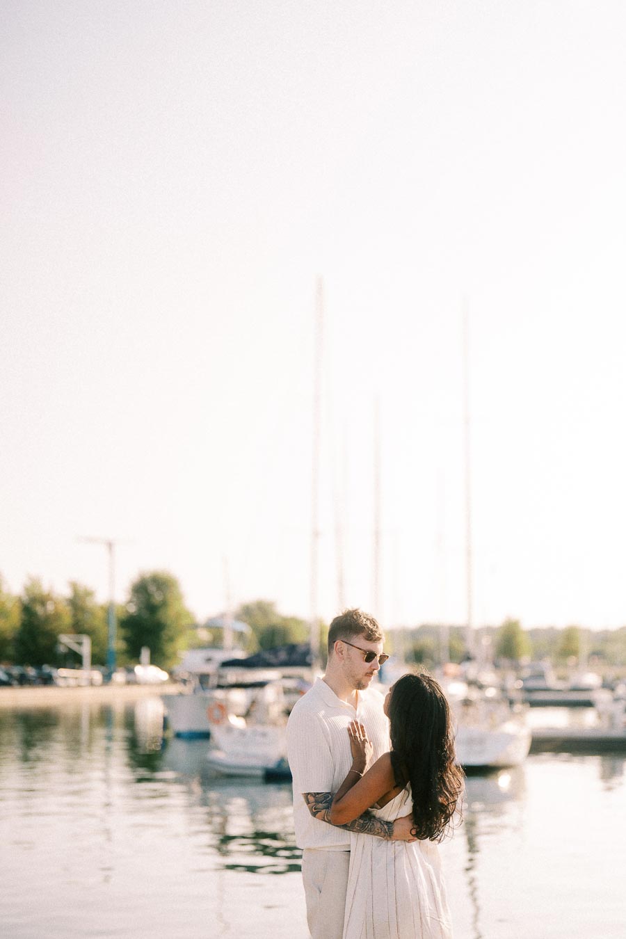 Amber and Devin embrace by sailboats at Royal Hamilton Yacht Club during golden hour.