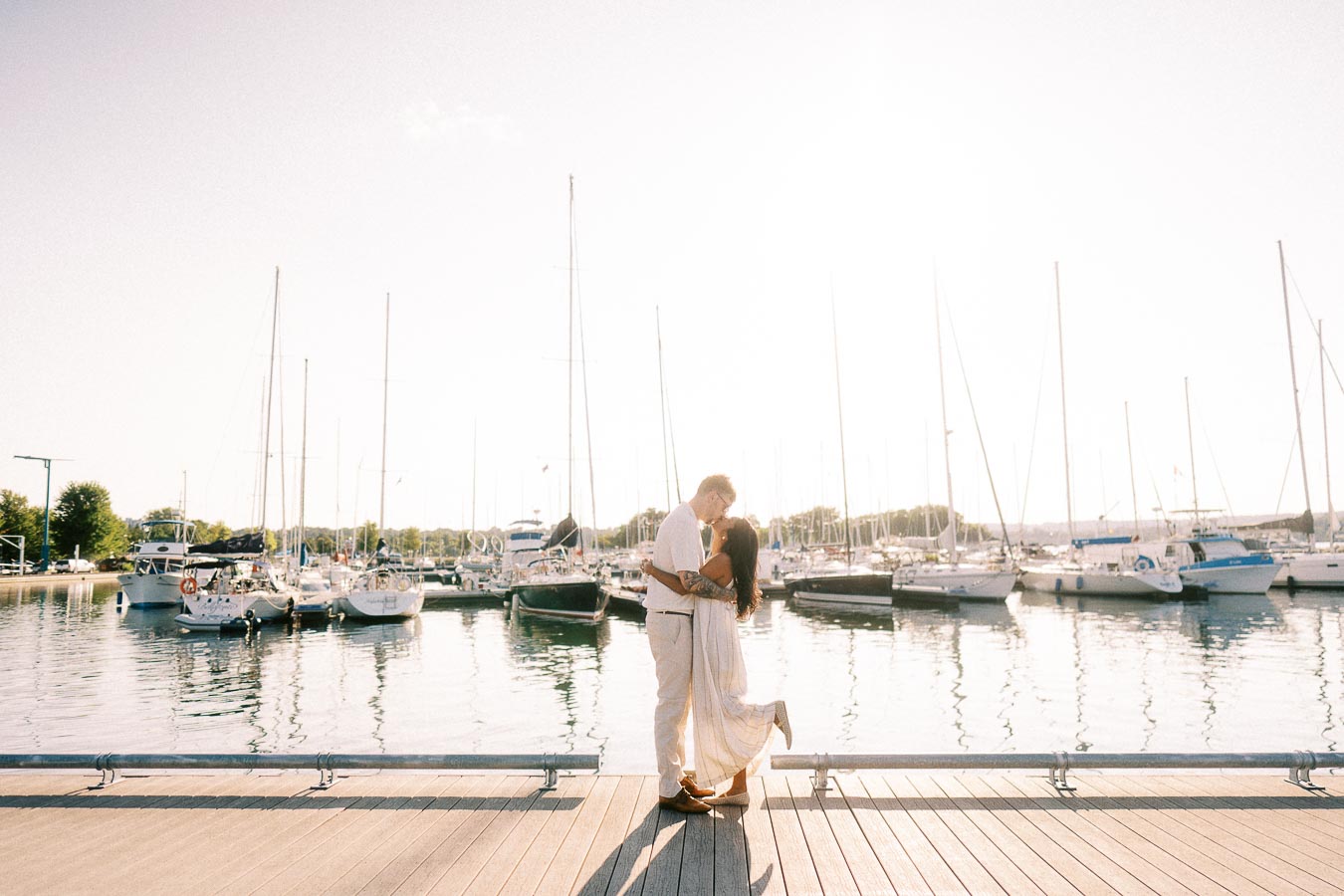 Amber and Devin embrace on a marina dock with sailboats at sunset in Hamilton, Ontario.
