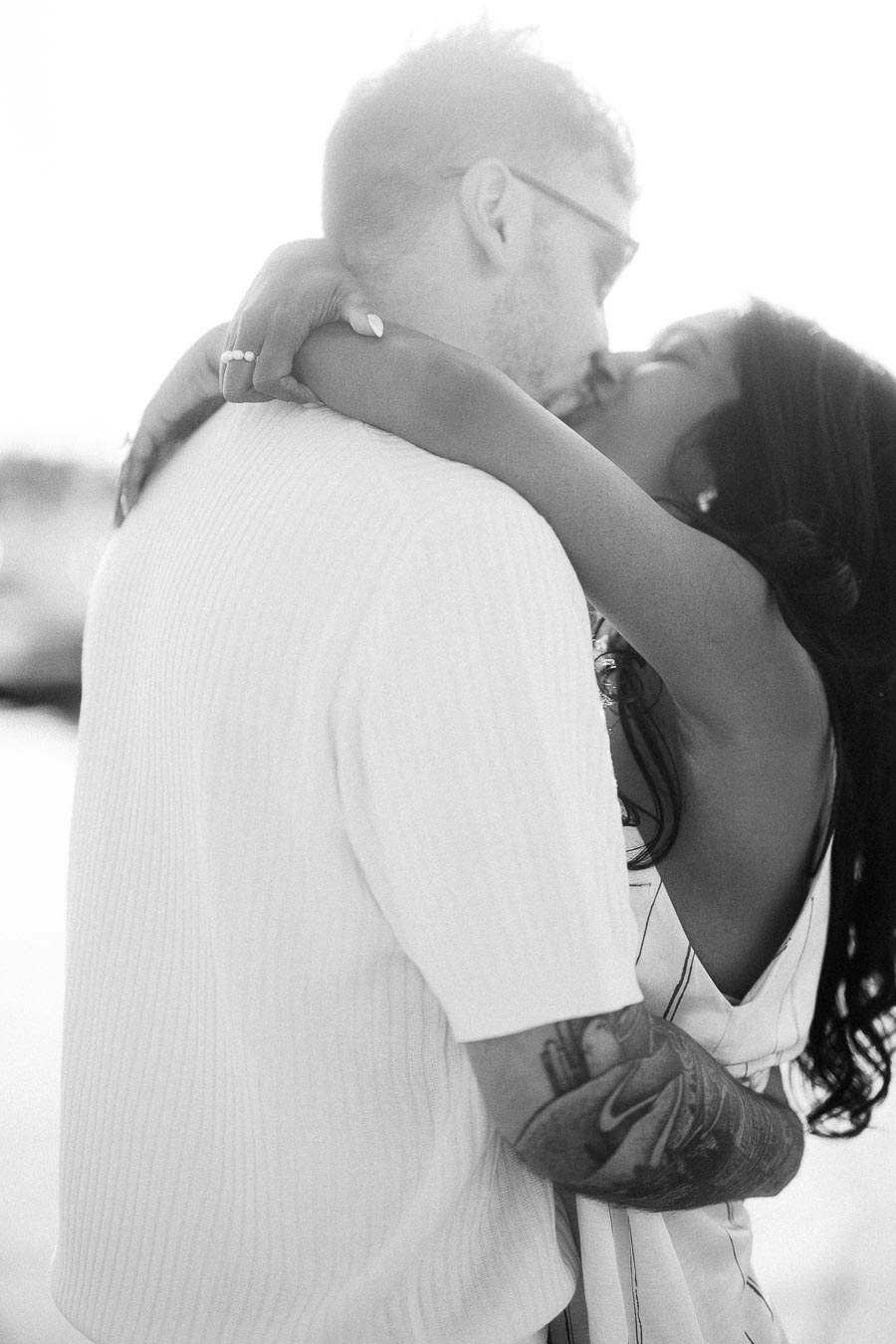 Amber and Devin kissing in a soft black-and-white engagement portrait near the waterfront.