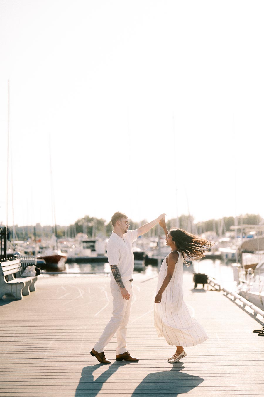 Amber and Devin twirl on a marina dock during a golden hour engagement session in Hamilton.