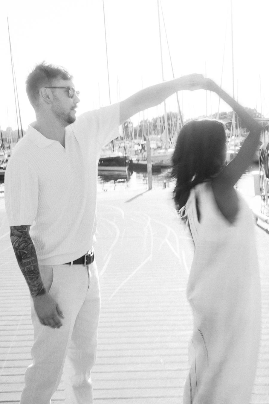 Amber and Devin twirl on a marina dock during a black-and-white engagement session in Hamilton.