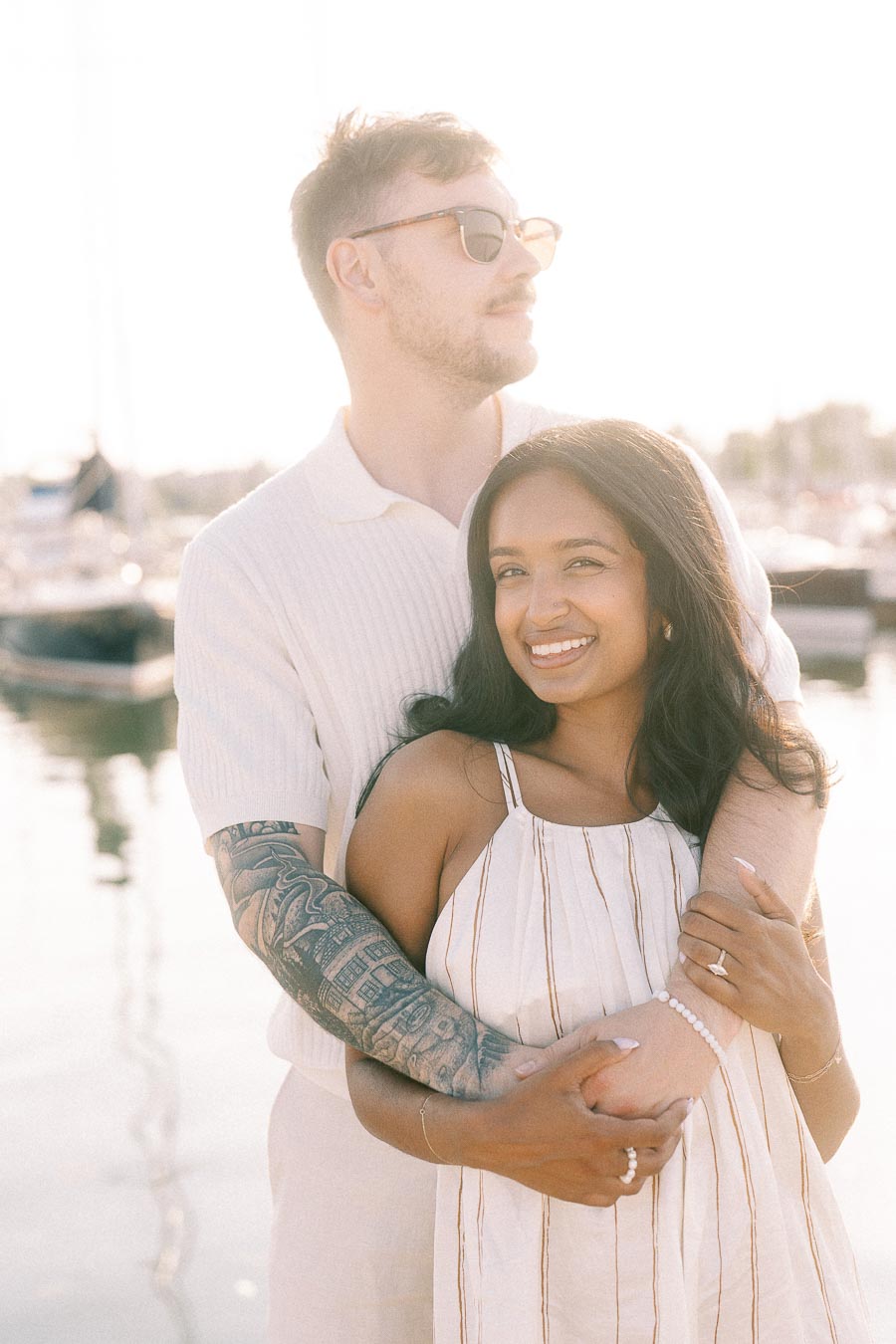 Amber and Devin embracing at a marina during a bright golden hour engagement session.