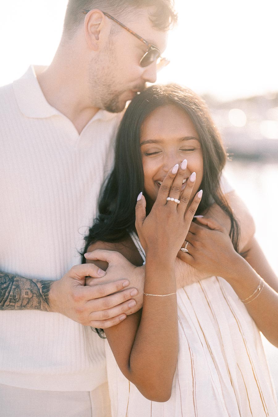 Devin kisses Amber’s forehead as she smiles with her engagement ring at the waterfront.