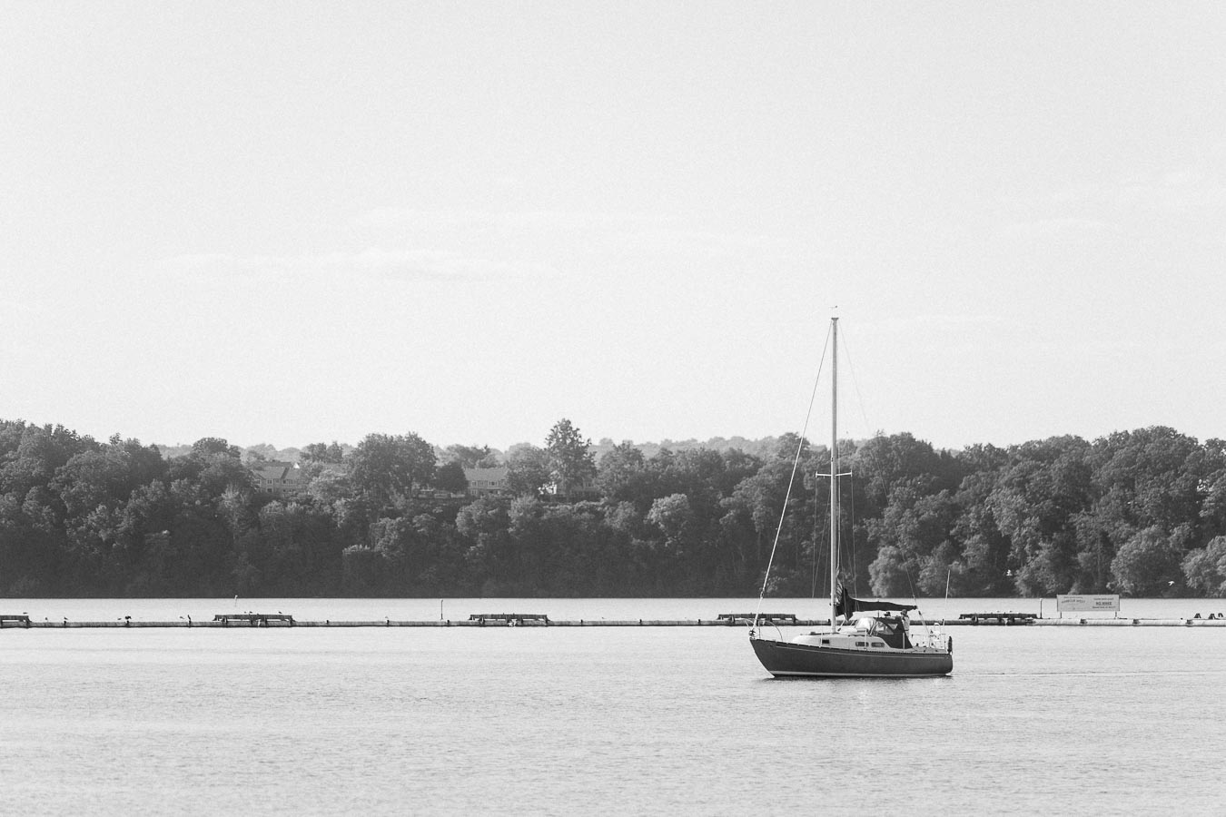 Black-and-white sailboat on calm Lake Ontario water near the Hamilton shoreline.