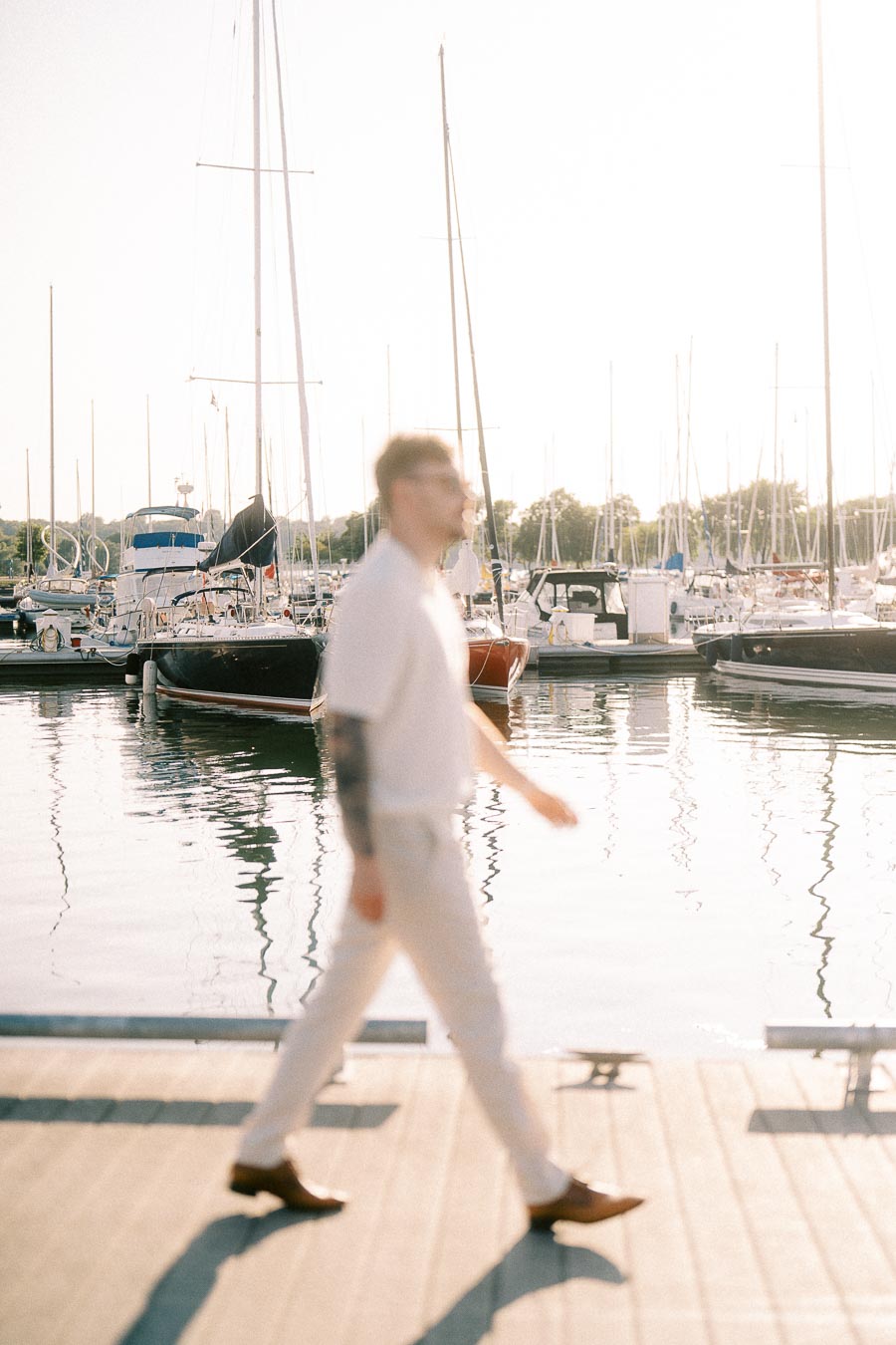 Man walking on a marina dock with sailboats behind him at golden hour in Hamilton, Ontario.